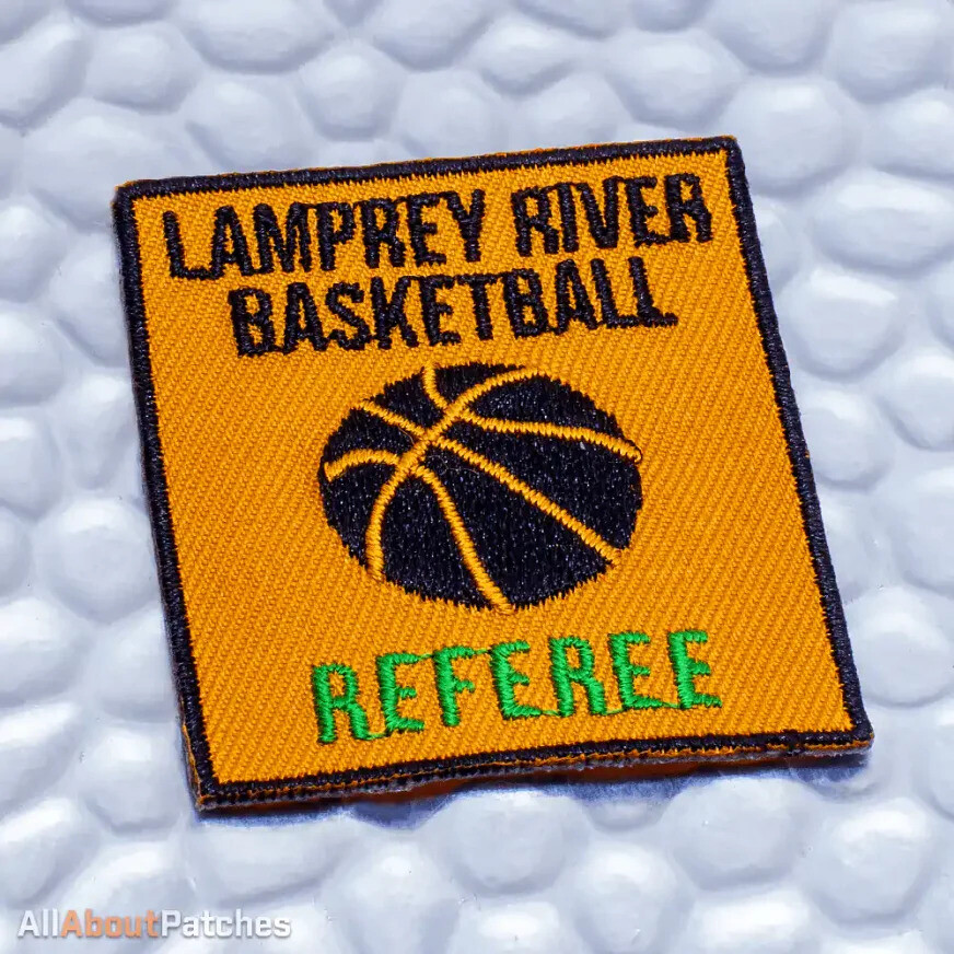 Square gold patch with a black basketball and green lettering, on white bubble wrap
