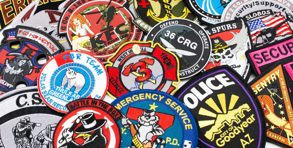 Pile of embroidered and PVC patches in many shapes and colors, overlapping on a white surface